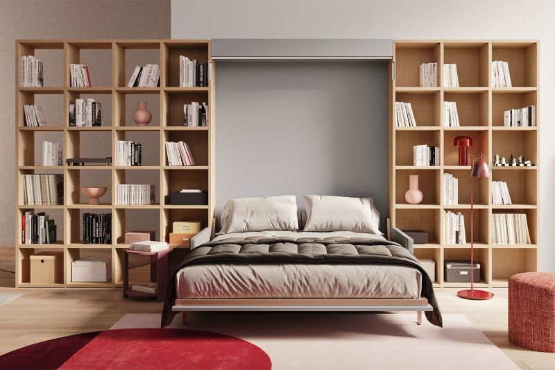 Monolocale con grande libreria divisoria doppia in legno chiaro e letto trasformabile matrimoniale aperto