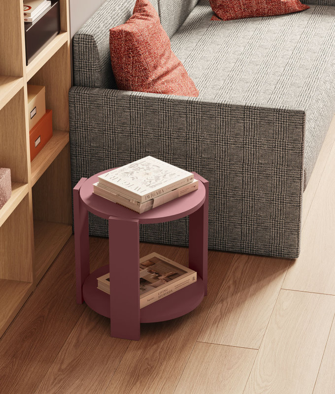Tavolino-comodino rosa posizionato accanto a un divanetto richiudibile in tessuto grigio